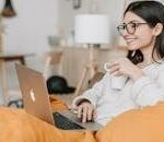 Woman enjoying a cozy moment with a laptop and coffee in a modern interior setting.